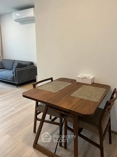 Modern living room with wooden dining table and cozy gray sofa, featuring sleek air conditioning unit.