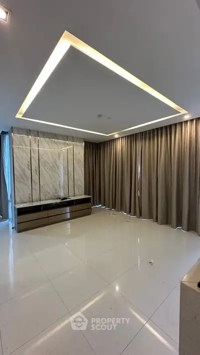 Spacious modern living room with elegant ceiling lighting and floor-to-ceiling curtains.