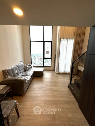 Spacious living room with large windows and modern staircase in a high-rise apartment.