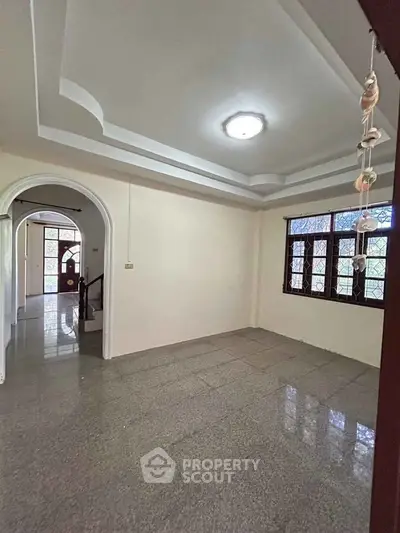 Spacious living area with elegant archway and large windows in a charming home.