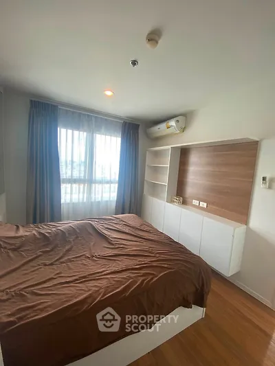 Cozy bedroom with wooden flooring and built-in storage, featuring a large window for natural light.