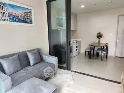 Modern living room with cozy sofa and open kitchen layout, featuring a washing machine and dining area.