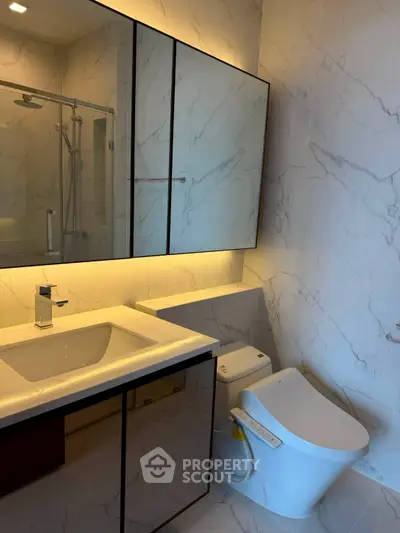 Modern bathroom with sleek fixtures and marble walls, featuring a stylish toilet and illuminated mirror.