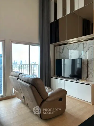 Modern living room with city view, featuring sleek TV setup and comfortable leather seating.