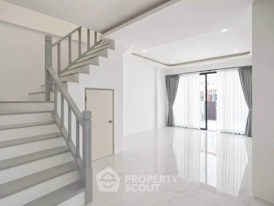 Spacious modern living room with elegant staircase and large windows for natural light.