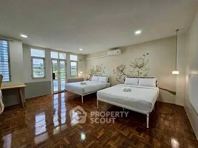 Spacious bedroom with two beds and elegant floral wall design, featuring wooden flooring and ample natural light.
