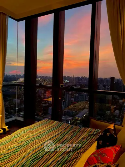 Stunning bedroom with panoramic city view and vibrant sunset.