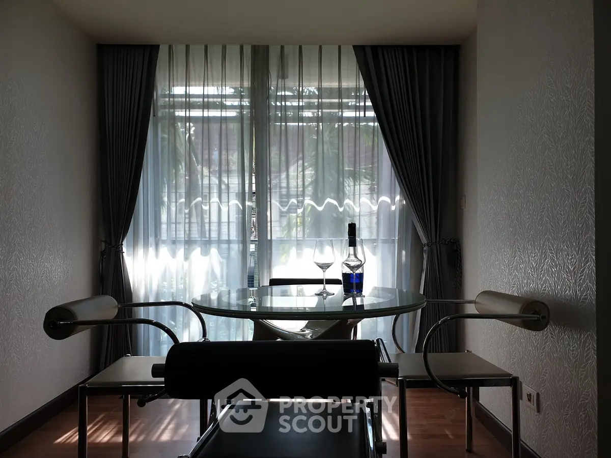 Elegant dining area with glass table and chairs, featuring a scenic view through large windows.