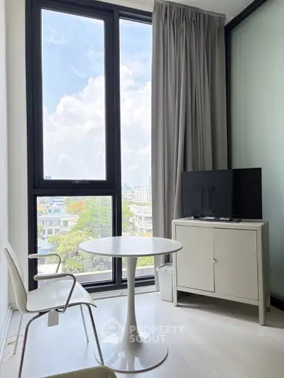 Bright modern living room with large windows and city view, featuring minimalist furniture and a TV stand.