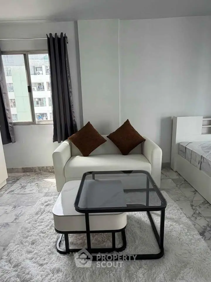 Modern living room with white sofa, glass coffee table, and large window in a stylish apartment.