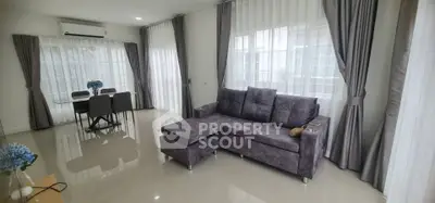Spacious modern living room with elegant gray sofa and dining area, featuring large windows and stylish curtains.