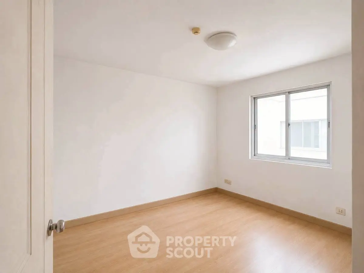 Spacious empty room with wooden flooring and large window, perfect for customization.