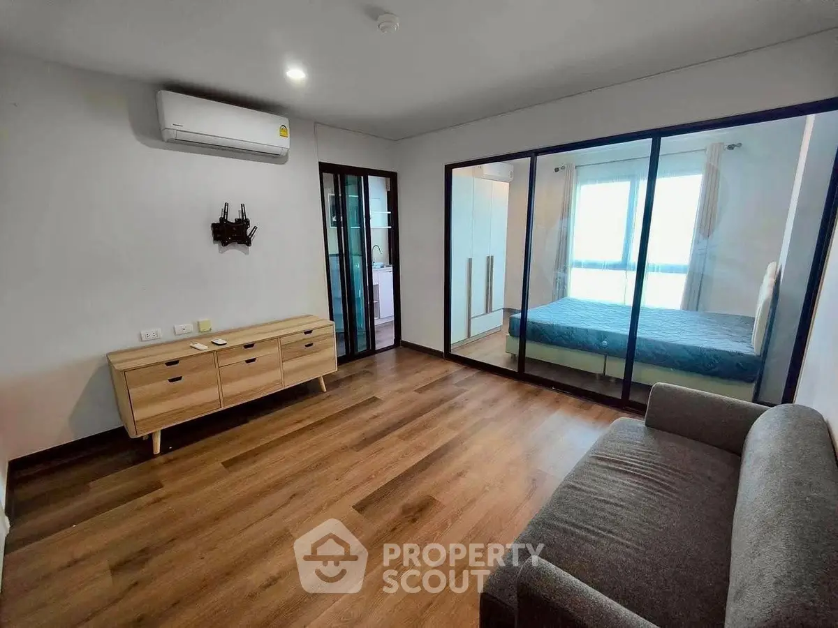 Modern apartment with spacious living room and glass partitioned bedroom, featuring sleek wooden flooring.