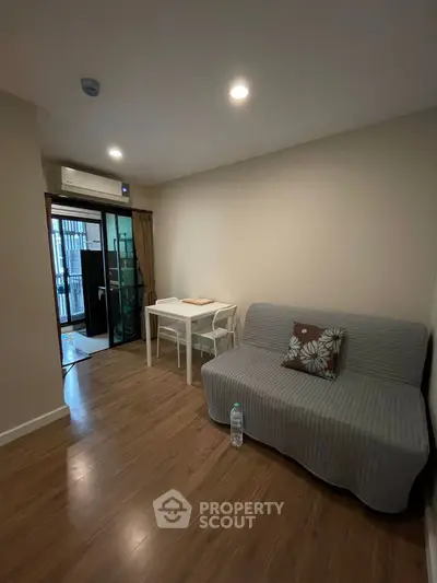 Cozy living room with sofa and dining table, featuring wooden flooring and balcony access.