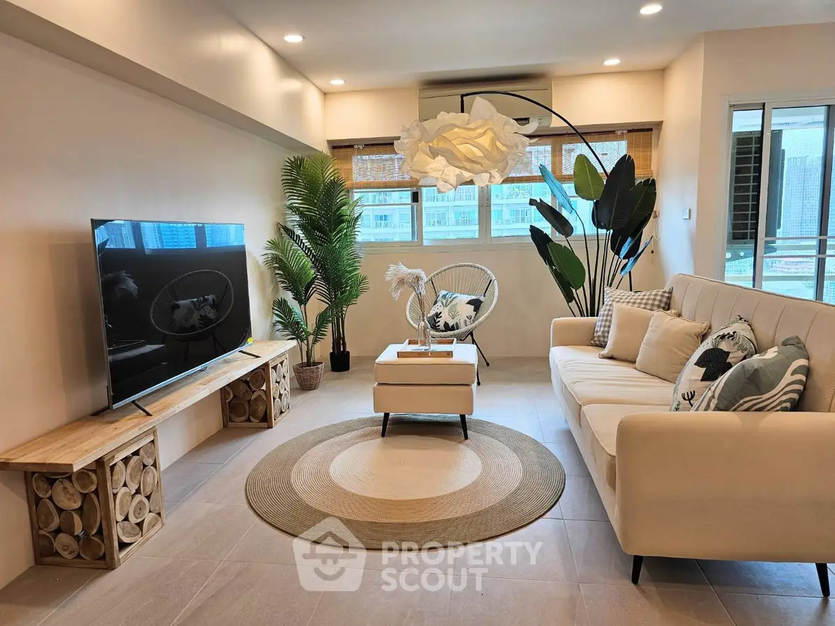 Modern living room with stylish decor, large TV, and natural light from balcony.