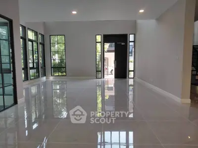 Spacious modern living room with large windows and glossy tiled floors, offering abundant natural light.