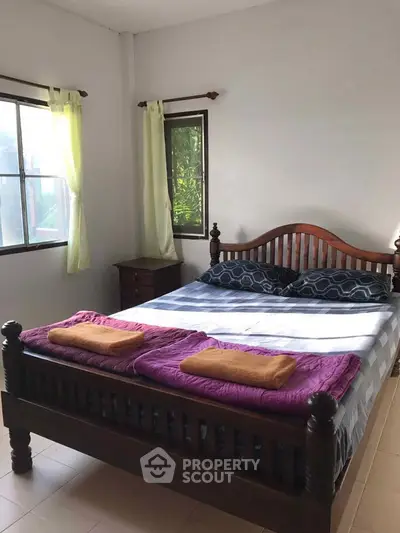 Cozy bedroom with wooden bed frame and natural light from two windows.