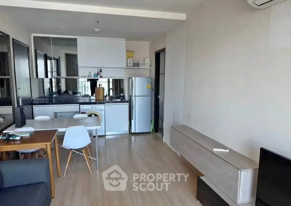 Modern open-layout living room with compact kitchen and dining area, featuring sleek furniture and natural light.