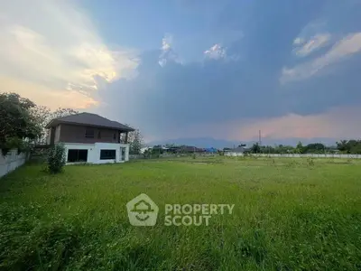 Expansive green field with a distant view of a house and scenic sky backdrop.