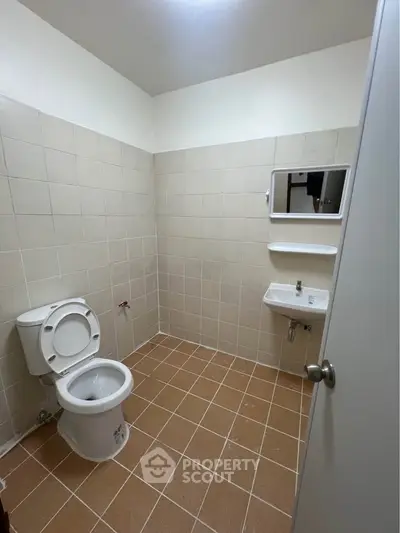 Spacious bathroom with tiled walls and floor, featuring a toilet and sink.