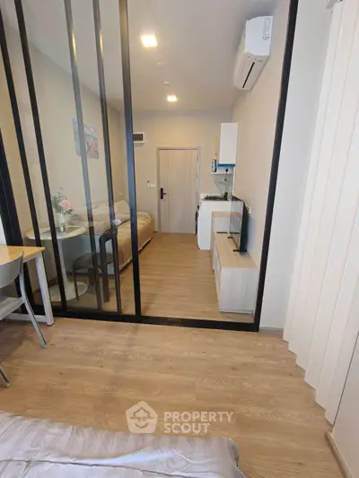 Modern studio apartment with open layout and stylish glass partition, featuring cozy living area and compact kitchen.