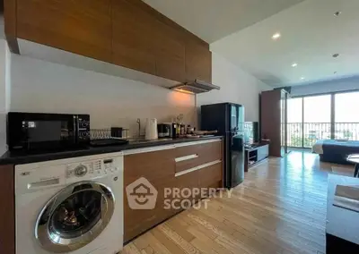 Modern open-layout kitchen with washing machine and spacious living area with balcony view.