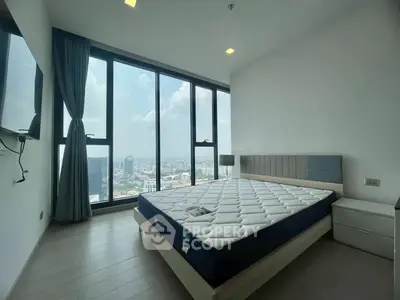 Spacious bedroom with floor-to-ceiling windows offering stunning city views, modern furnishings, and ample natural light.