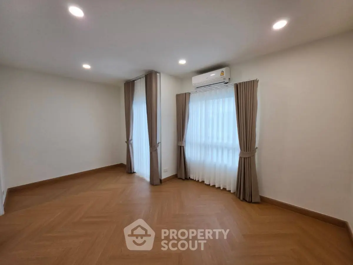 Spacious empty room with elegant wooden flooring and large windows with curtains.