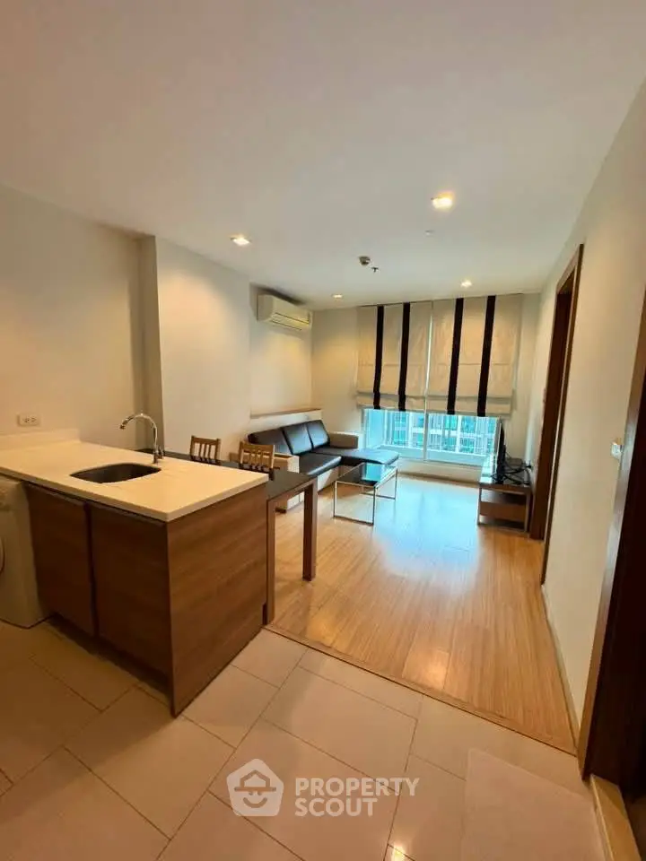 Modern open-layout living room with kitchen, featuring wooden flooring and ample natural light.