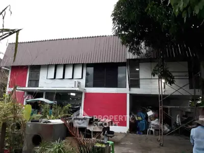 Unique two-story building with red and white facade, surrounded by lush greenery and outdoor storage area.