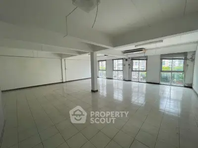 Spacious open-plan room with large windows and tiled flooring, ideal for versatile use.