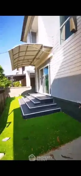 Modern house exterior with steps leading to glass doors and lush green lawn