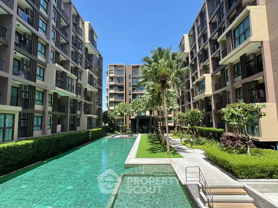 Modern apartment complex with pool and lush landscaping under clear blue sky.