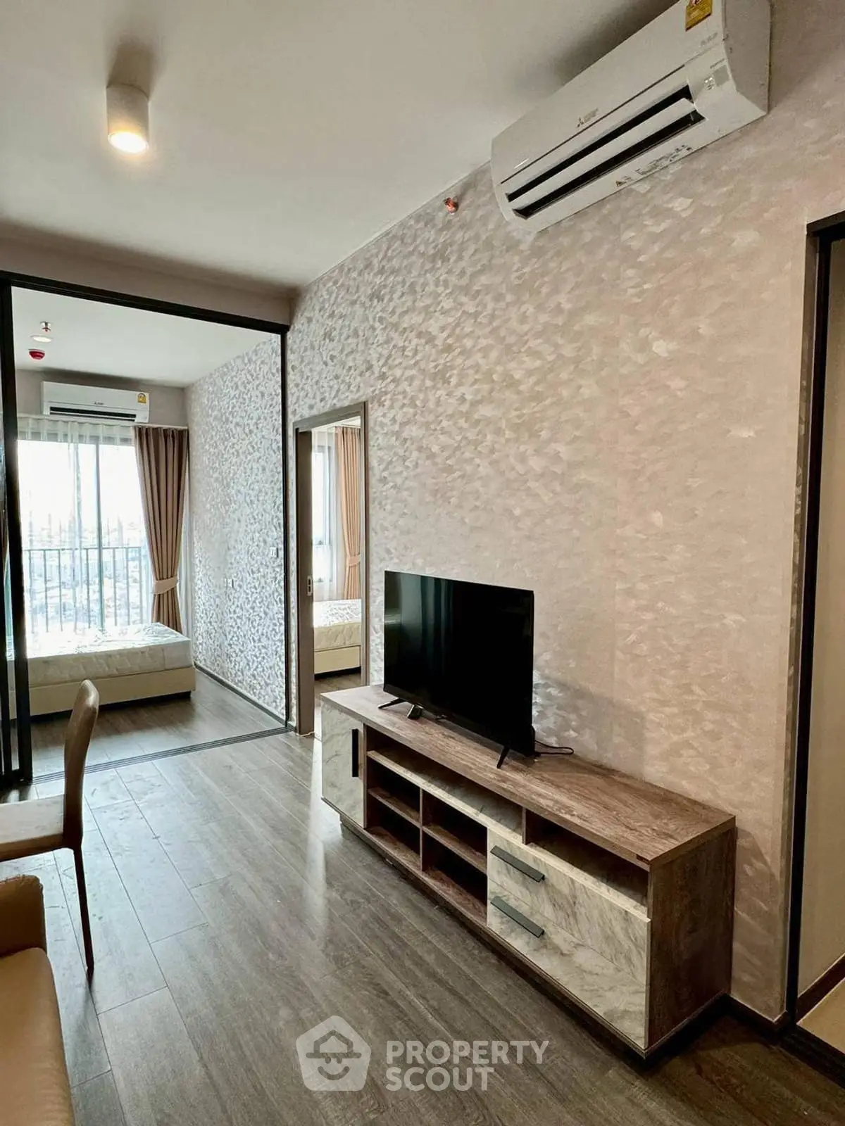 Modern living room with TV and air conditioning, featuring a view into a cozy bedroom.