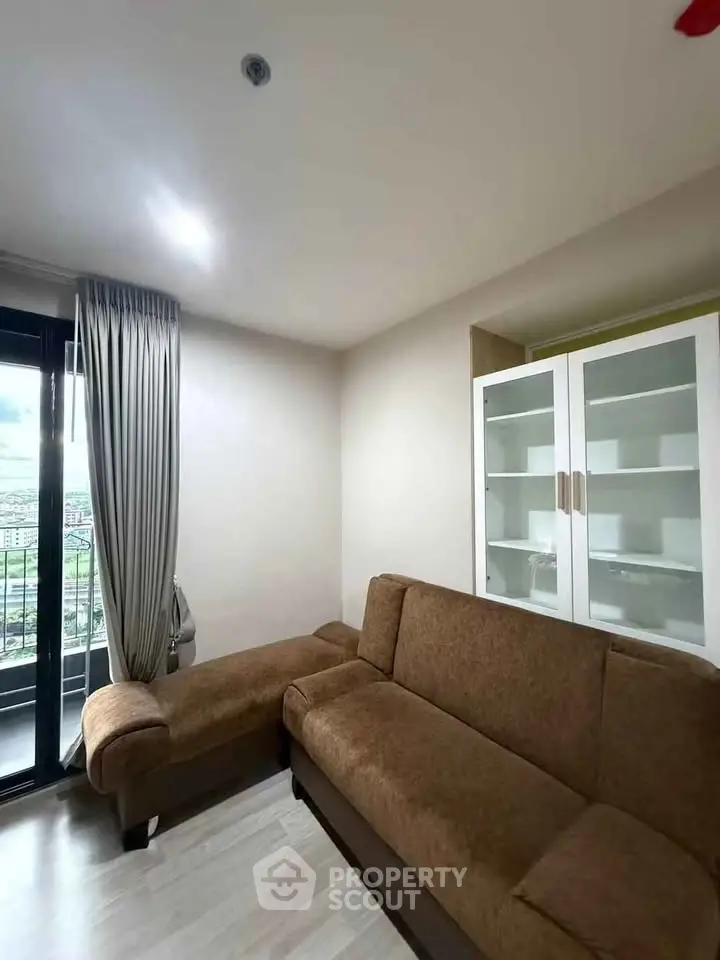 Modern living room with brown sofa and glass cabinet, featuring a balcony view.