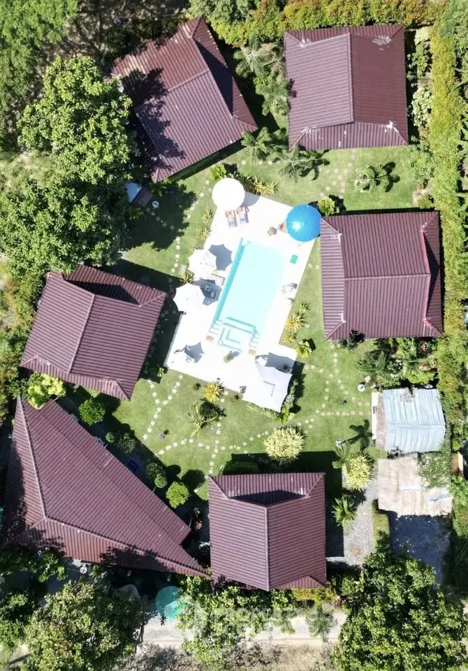 Aerial view of a luxurious property with multiple villas surrounding a central pool, lush greenery, and outdoor seating.