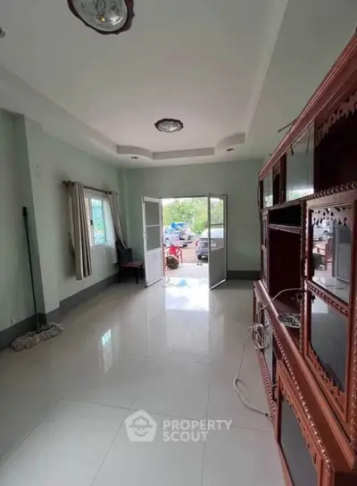 Spacious living room with elegant wooden cabinet and open door to garden view.