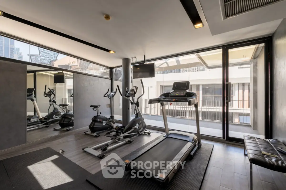 Modern gym with exercise equipment and large windows in a luxury building.