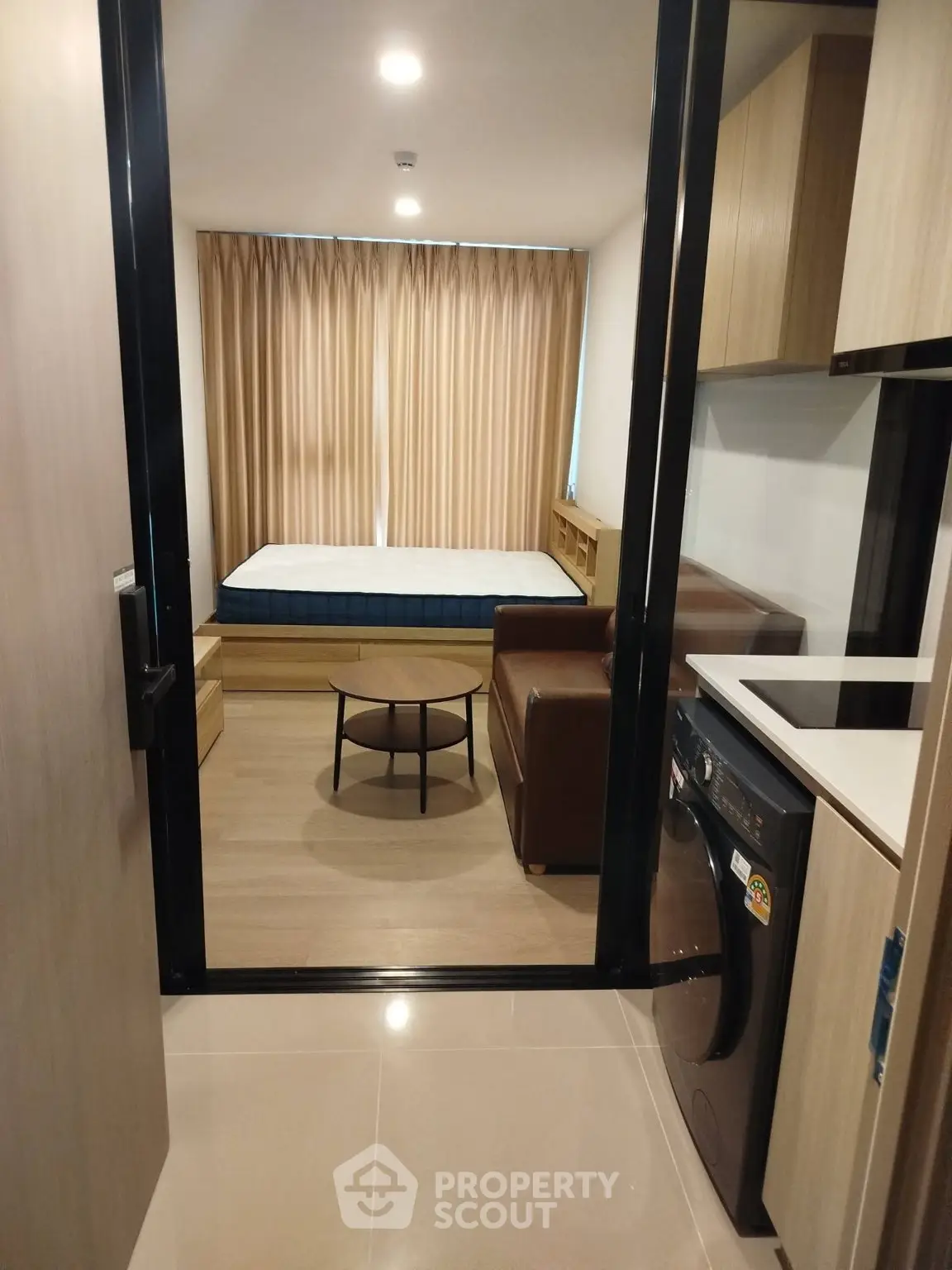 Modern studio apartment with cozy living area and compact kitchen featuring a washing machine.