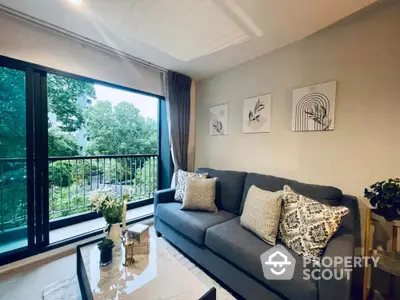 Modern living room with large window and stylish decor overlooking lush greenery.