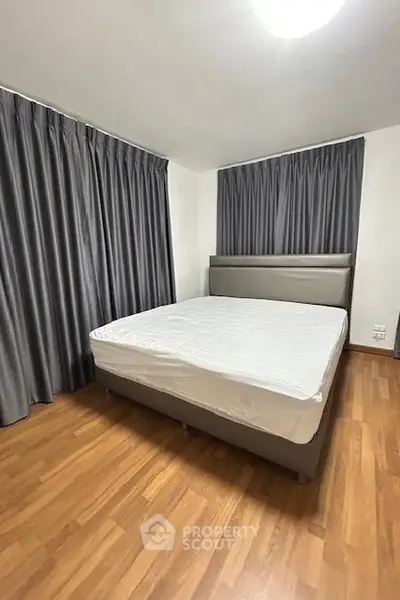 Spacious bedroom with elegant wooden flooring and large windows with curtains.