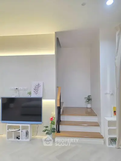 Modern living room with sleek staircase and mounted TV, featuring minimalist decor and soft lighting.