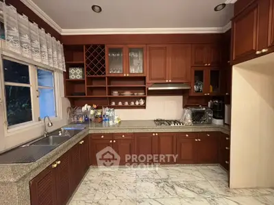 Spacious kitchen with wooden cabinets and marble flooring, featuring a gas stove and ample storage.