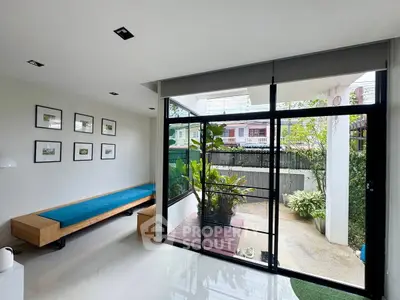 Modern living room with large glass doors opening to a lush garden patio, featuring minimalist decor and natural light.