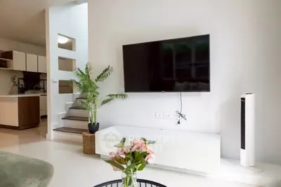 Modern living room with wall-mounted TV, stylish decor, and open kitchen layout.