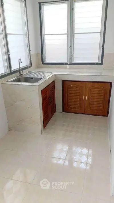 Bright kitchen with tiled floor and wooden cabinets under large windows.