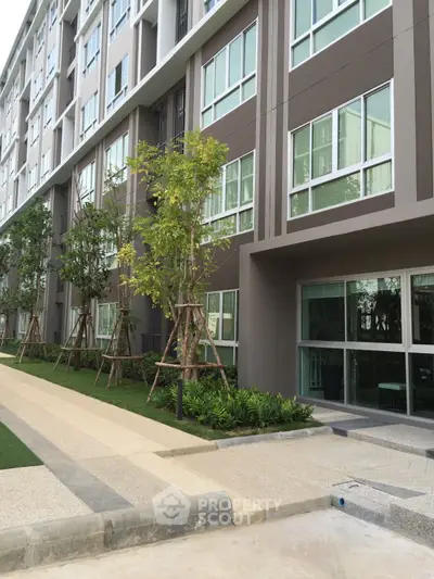 Modern apartment building exterior with landscaped entrance and young trees.