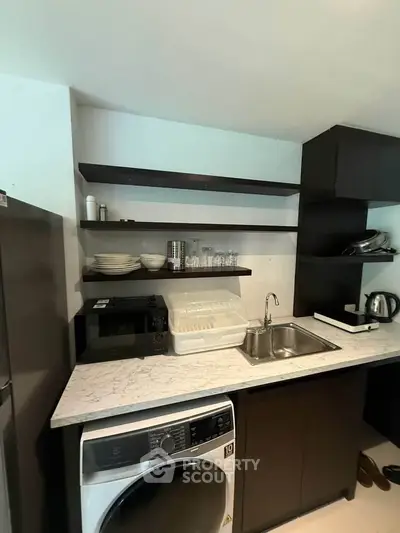 Modern kitchen with sleek black cabinets and marble countertop featuring a washing machine and open shelving.