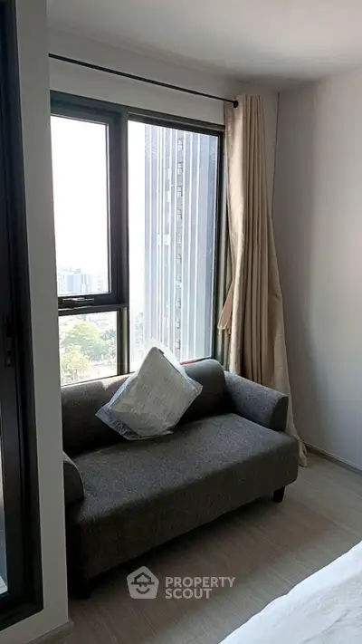 Cozy bedroom with city view, featuring a stylish gray sofa and large windows for natural light.