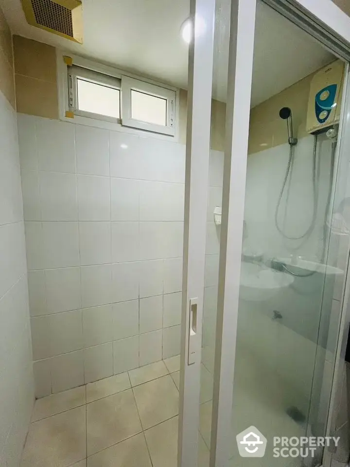 Modern bathroom with glass shower door and tiled walls, featuring a compact design and overhead shower.